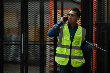 Storehouse male manager in reflective jacket talking on mobile phone while standing in a retail warehouse