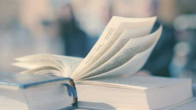 An open Bible lies on the table outside in the daytime wind. Open Torah book in the wind.