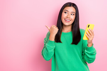 Photo portrait of dreaming interested korean lady wear green jumper hold phone look direct finger mockup new app isolated on pink color background