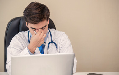 Overworked young doctor man sit office. Displease caucasian health care worker using computer...