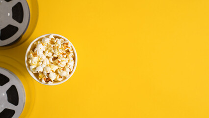 Cinema leisure and entertainment concept banner with copy space. Top view cup of popcorn and film reel on yellow background with blank space for advertising