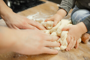 Parent with baby together knead raw elastic dough on kitchen tabletop closeup. Little hands help...