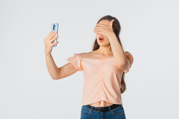Shocked young woman looks excited at mobile phone, surprised reaction on smartphone screen, cover eyes with hand shocked with shame for mistake, expression of fear