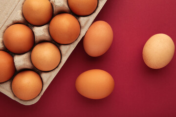 Chicken eggs in an open egg carton on red background. Top view with copy space. Natural healthy food and organic farming concept.