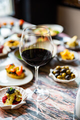 glass with red wine and wine snack set, food from spain, cheese, meat, vegetables and other appetizers on table
