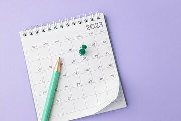 Calendar with pinned date and pen and clock on pastel purple background, top view