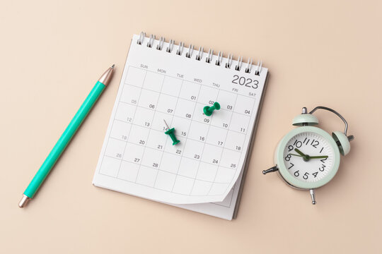 Calendar with pen and clock on pastel beige background