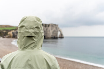Rückenansicht einer Frau mit Kapuze, die auf Felsen der Normandie blickt 