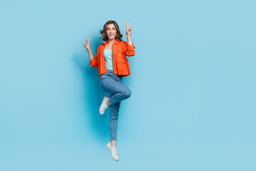 Fototapeta na wymiar Full size photo of young pretty girl jumping excited showing double v-sign dressed stylish orange clothes isolated on blue color background