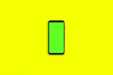 Phone with vertical green screen with chroma key isolated yellow background. Mock Up Display. Smartphone gadget for advertising. Top above view. Mobile phone with empty blank screen. Layout template