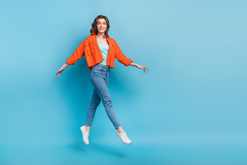 Fototapeta na wymiar Full size photo of young pretty girl jumping walking elegant soar hover wear trendy orange outfit isolated on blue color background