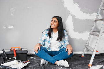 Young smiling Indian woman sits on floor taking a break home DIY