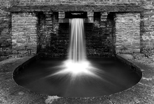 Small artificial cascade in Iserlohn Sauerland Germany near “Rupenteich“, a pond in an old park and recreation area with natural creeks and historic brick walls. Longtime exposure, black and white.