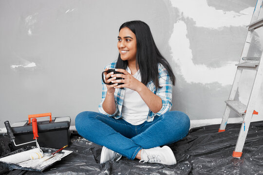 An attractive young Indian woman sits on the floor taking coffee break from DIY