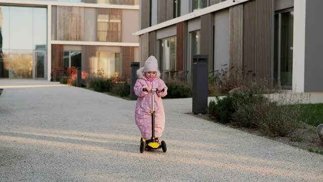 Adorable toddler girl riding a children's scooter on the street