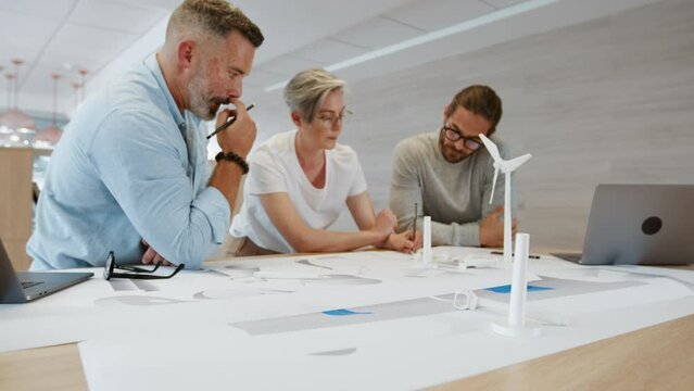 Creative business people working together in an office, designing a wind turbine using 3D drawings and models. Engineering team discussing and contributing ideas towards a sustainable energy project.