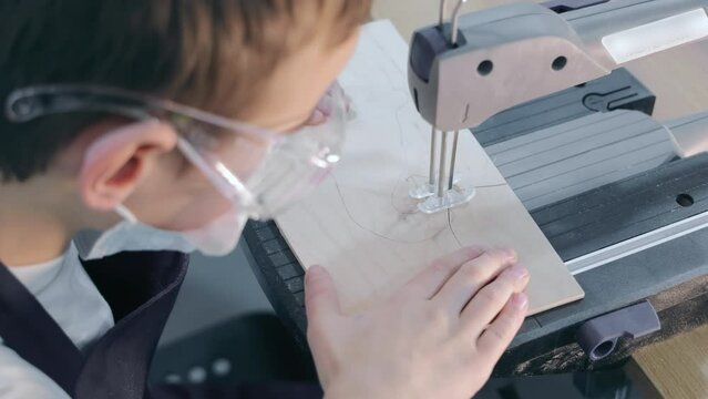 A child at a cool crafts class saws a pattern from plywood