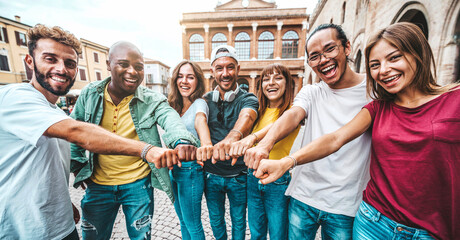 Multi ethnic group of young people making fist bump as symbol of unity, community and solidarity - Happy friends portrait standing outdoors - Teamwork join hands and support together