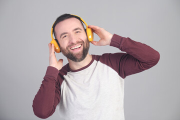 Young man listening to music with yellow wireless headphones in a studio shot - 565302938