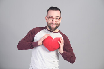 Young man holding a small red heart shaped pillow while looking at camera - 565302956