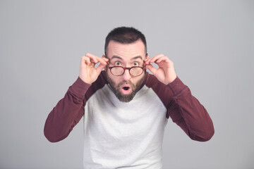 Surprised young man with open mouth grabbing his glasses looking at camera in a studio shot - 565302992