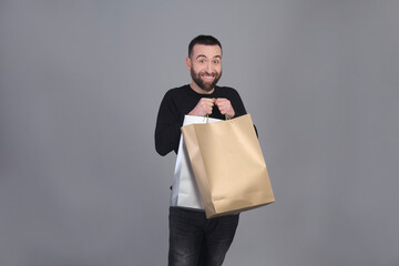 Young man holding shopping bags on shoulder while looking at camera - 565303143