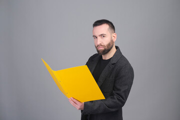 A businessman holding a yellow open folder while looking at the camera - 565303177