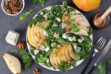 Salad with arugula, pear, dor blue cheese, honey and walnuts in plate on gray table