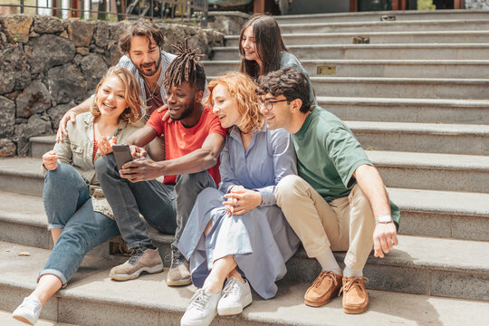group of diverse z generation people sitting on staircase playing with cell phone
