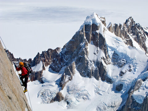 A climber climbs the steep  north face of Torre Egger, with the peaks of Cerro Rincon and the glaciers of the Southern Patagonia