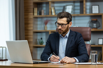 Fototapeta na wymiar Successful mature businessman working inside office, man in business suit working at workplace with documents and laptop, boss behind paperwork attentive and focused.