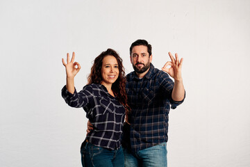 An adult couple doing ok sign with fingers while smiling and looking at camera against a white background - 565320590
