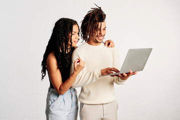 A couple of friends standing and using a laptop in a studio shot - 565320706