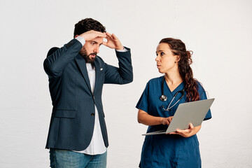 A female doctor showing bad news about diagnosis or test result with a laptop to patient man standing who grabs his head - 565320724