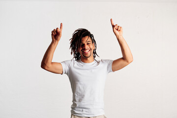 A smiling young man standing pointing both hands upwards as he looks at camera in a studio - 565320759