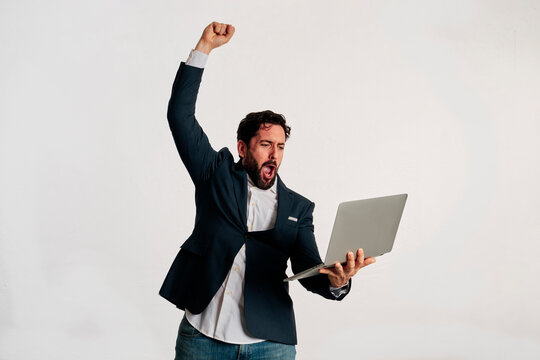 An euphoric businessman with a clenched fist raised and holding a laptop in studio with copy space