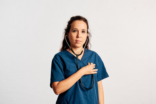 A doctor using her stethoscope on herself while looking at camera in a studio with copy space