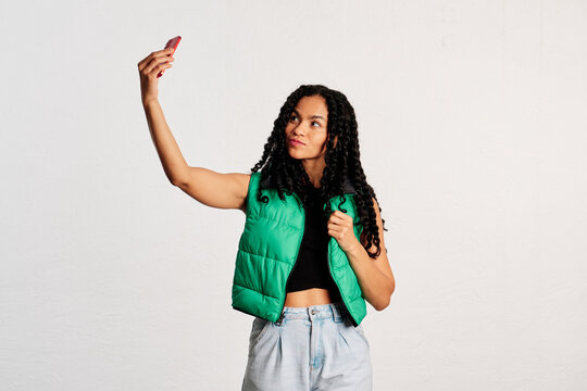Front view of a young woman taking a selfie in a studio