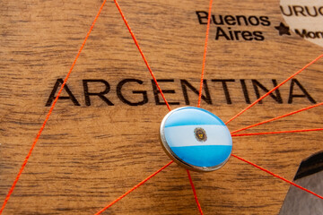 Argentina flag on the pushpin with red thread showed the paths of movement or areas of influence in the global economy on the wooden map. Planning of traveling or logistic concept. Network connection