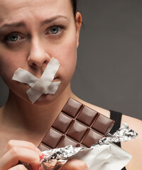 Diet concept: woman holding a chocolate with mouth sealed