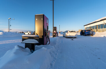 Petrol pump surrounded by snow and illuminated by early morning sunlight at a service station in...