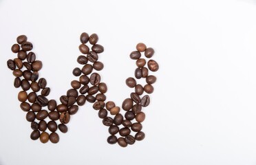 W is a capital letter of the English alphabet made up of natural roasted coffee beans that lie on a white background. Plenty of space to put text or pictures, top view and studio photography.