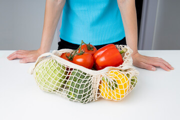 Standing woman near table with bag with fresh vegetables on white table