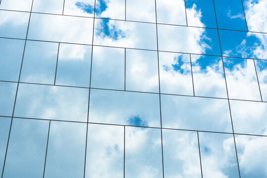 Blue Sky Reflection In Glass Facade Of Building. View Of Office Building Windows Close Up, Reflection And Perspective.. Glass Facade On A Sunny Day With Sunbeams On The Blue Sky.