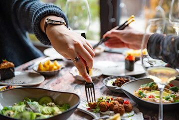 woman hand eating food in restaurant. wine, cheese, meat, vegetables and other appetizers on table