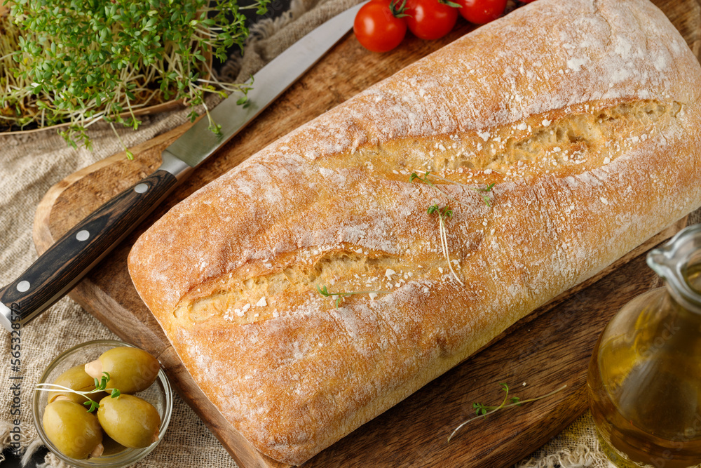 Wall mural fresh baked italian ciabatta wheat bread with knife, herbs, spices and olives on wooden board