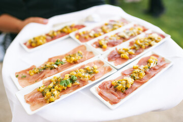 Waiter holding tray with tuna carpaccio served with mango and green herbs, catering for events