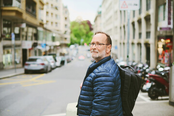 Outdoor portrait of 55-60 year old man wearing blue jacket and backpack, looking back over the...