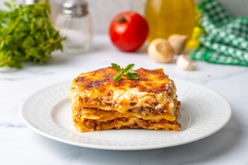 Portion of ground beef lasagna topped with melted cheese and garnished with fresh parsley served on a plate in close view for a menu