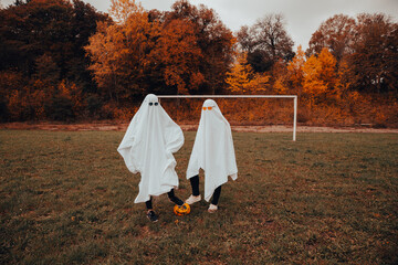 girls in ghost costumes for Halloween, football field in autumn

 